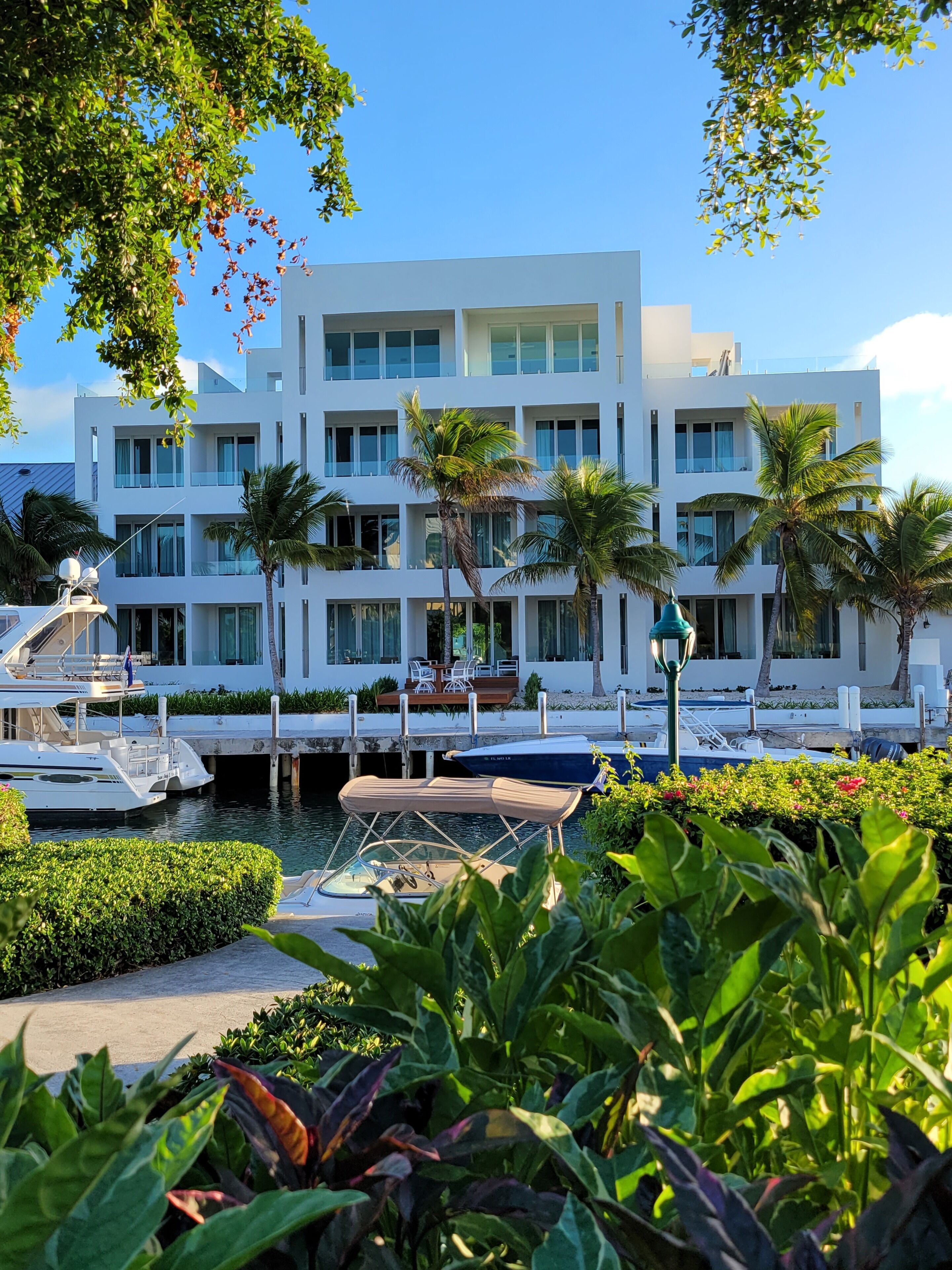 Un bâtiment moderne doté de nombreux balcons, un port de plaisance avec des bateaux et une végétation luxuriante.