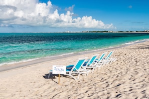 A beach with lounge chairs and a sign indicating property of ZENZA hotel.
