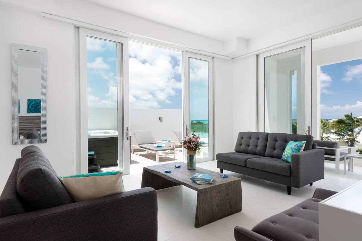 A modern living room with a grey sofa, a coffee table, and a view of the ocean through large glass doors.
