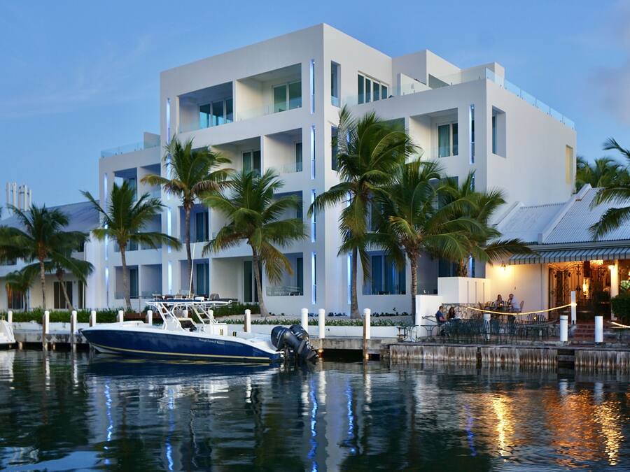 Een modern hotel met een boot voor de deur, omgeven door palmbomen en een rustige waterkant.