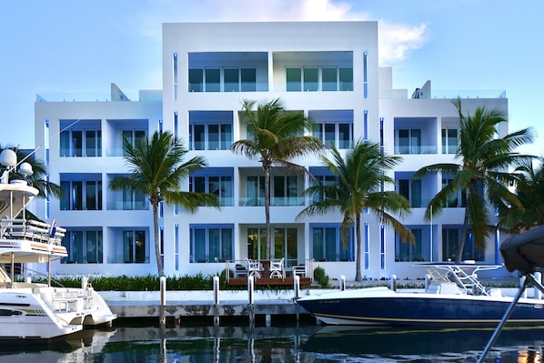 A modern multi-story building with a docked boat, palm trees, and a clear sky.