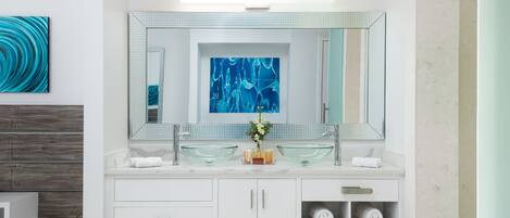 Une salle de bain moderne avec un meuble-lavabo blanc, deux vasques en verre, un grand miroir et un tableau abstrait bleu accroché au mur.
