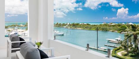 A balcony with white chairs and a view of a marina with boats and a clear blue sky.