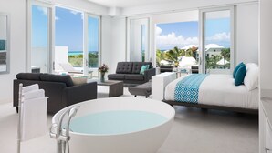 Quarto de hotel moderno com uma banheira grande, um sofá, uma cama e uma varanda com vista para o mar.