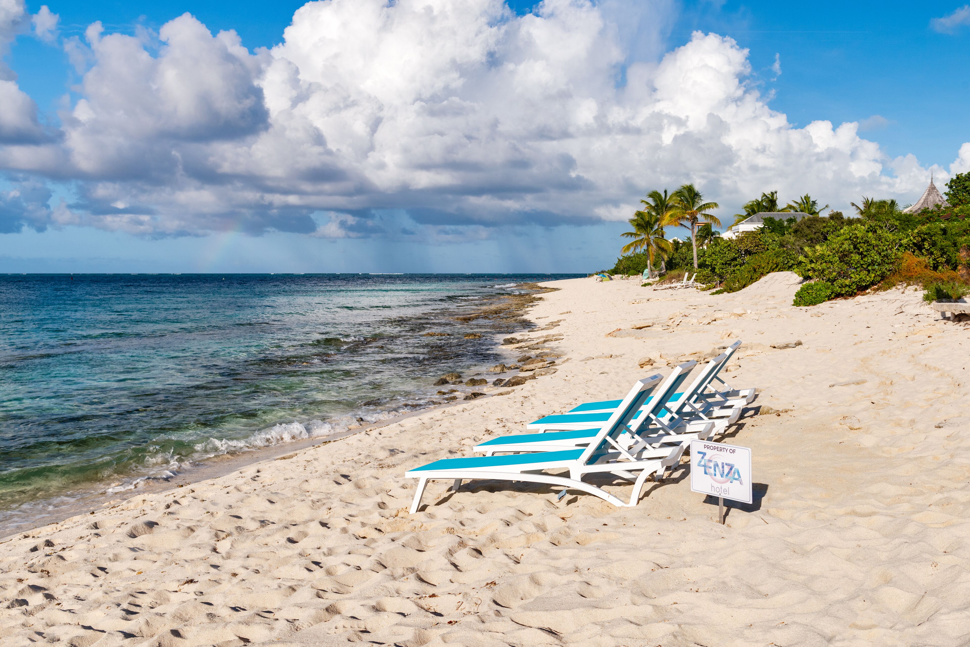A beach with white lounge chairs and a sign indicating property of ZENZA hotel.