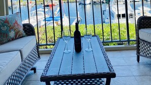 Un balcón con vista a un puerto deportivo, una botella de vino y dos copas sobre una mesa.