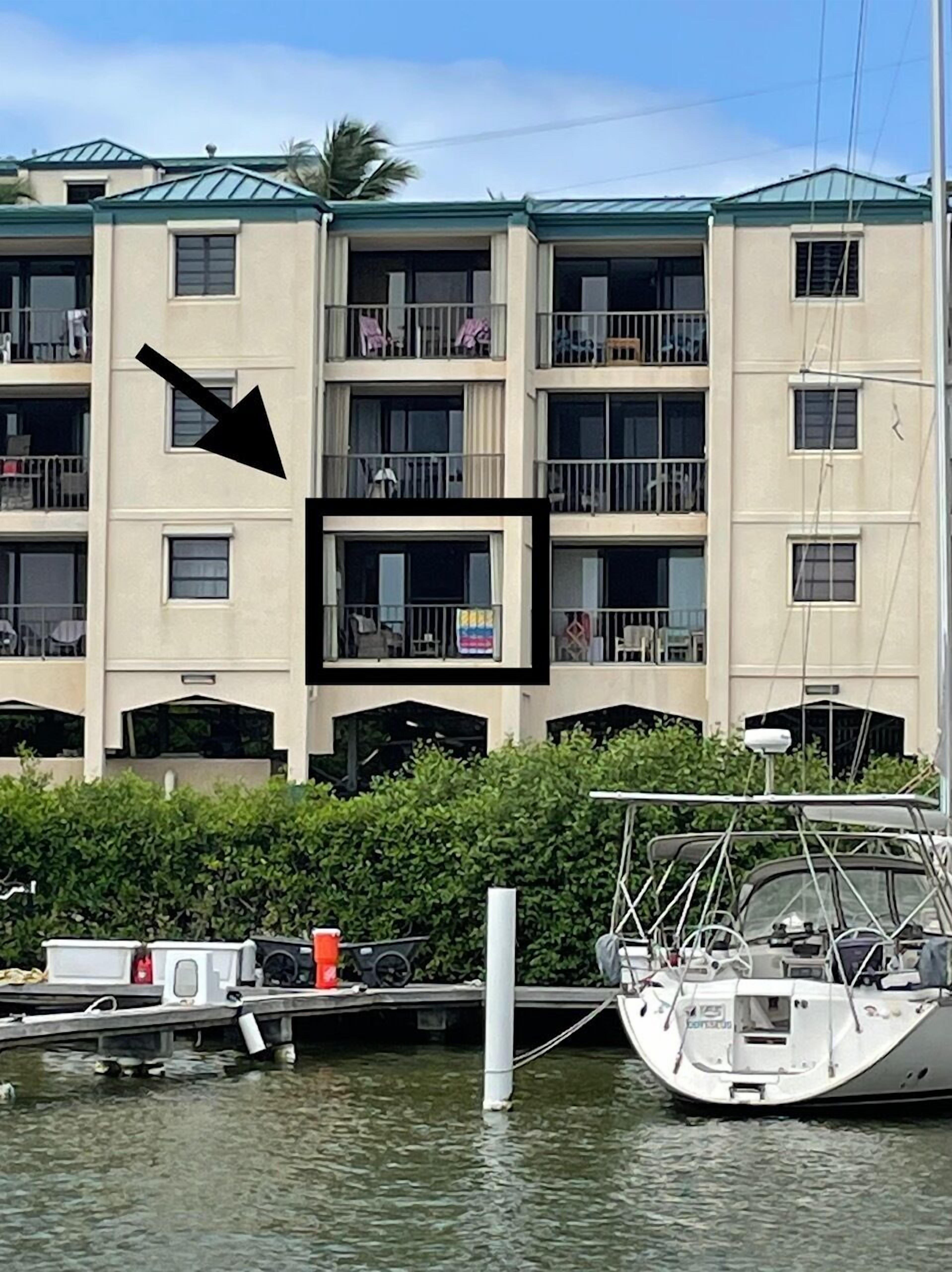 A multi-story building with balconies, a dock with boats, and a water body in front.