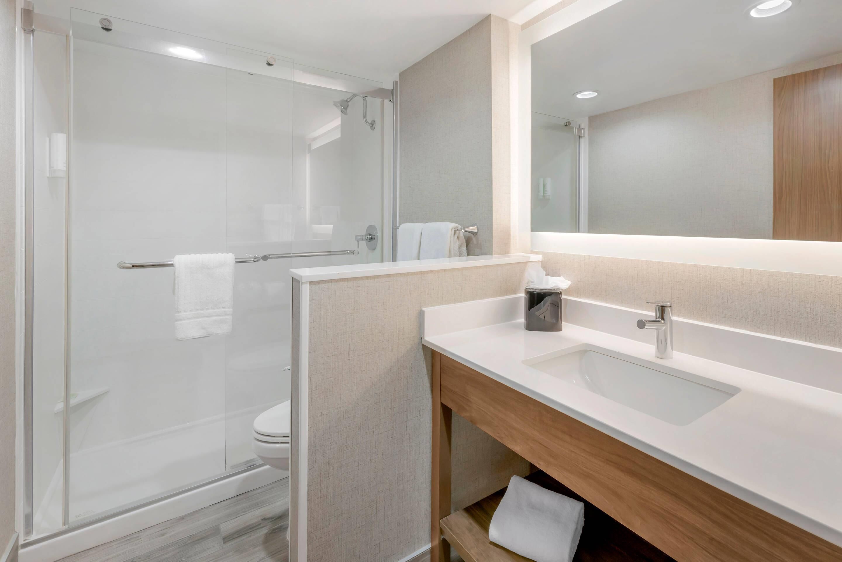 A modern bathroom with a glass-enclosed shower, a white sink, and a wooden vanity.
