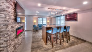 Un espace repas moderne avec un mur d’accent en pierre, une table en bois et des chaises bleues, des spots encastrés au plafond et un grand téléviseur fixé au mur.