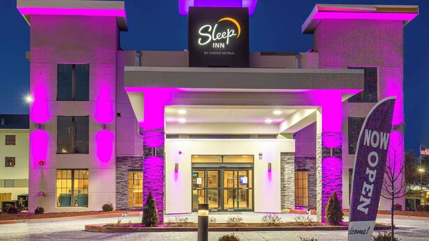 L’entrée d’un hôtel Sleep Inn, dotée d’un design moderne, avec une enseigne bien visible et une banderole accueillante.