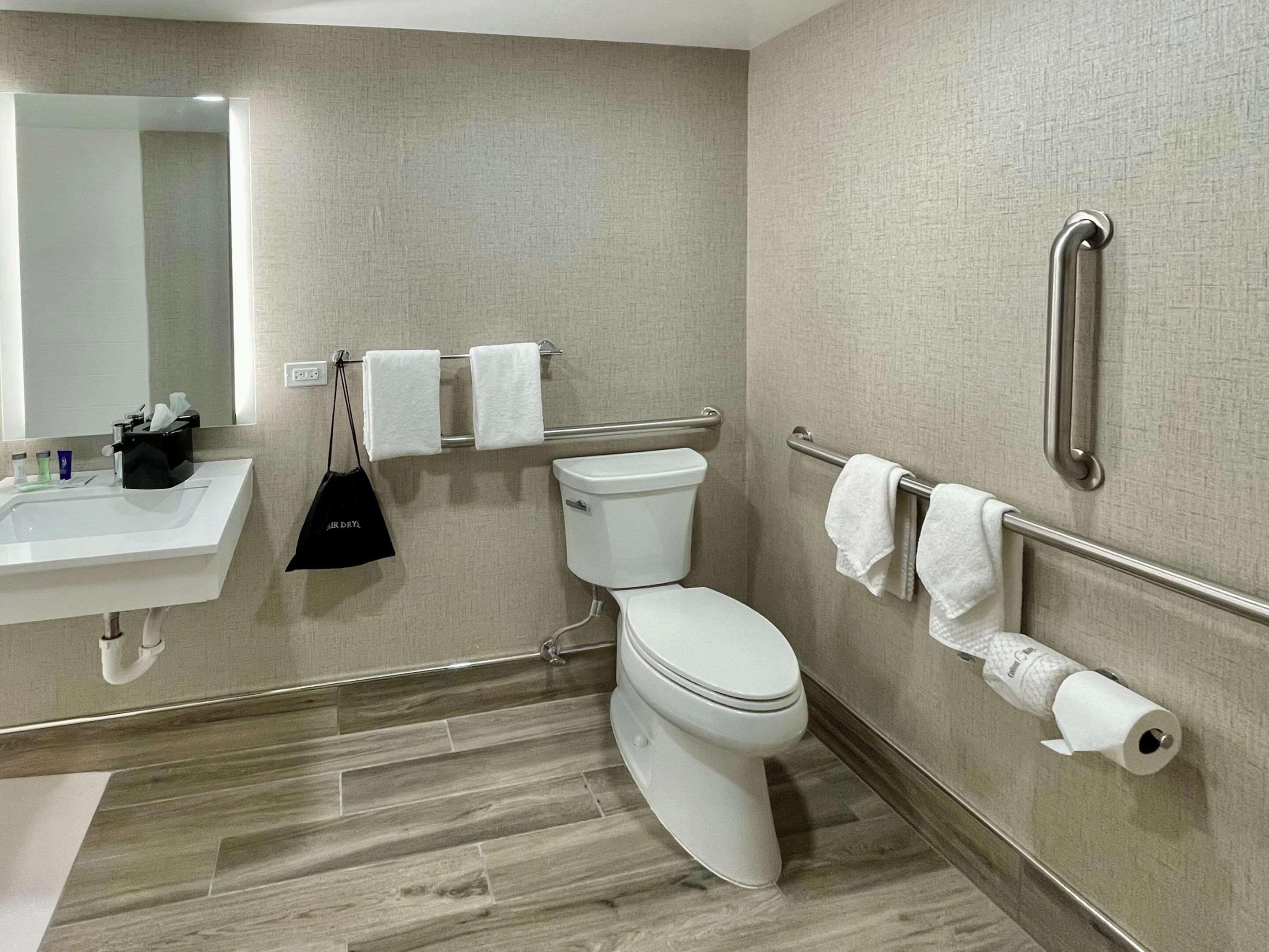 Un baño moderno con lavamanos, inodoro y barras de apoyo.
