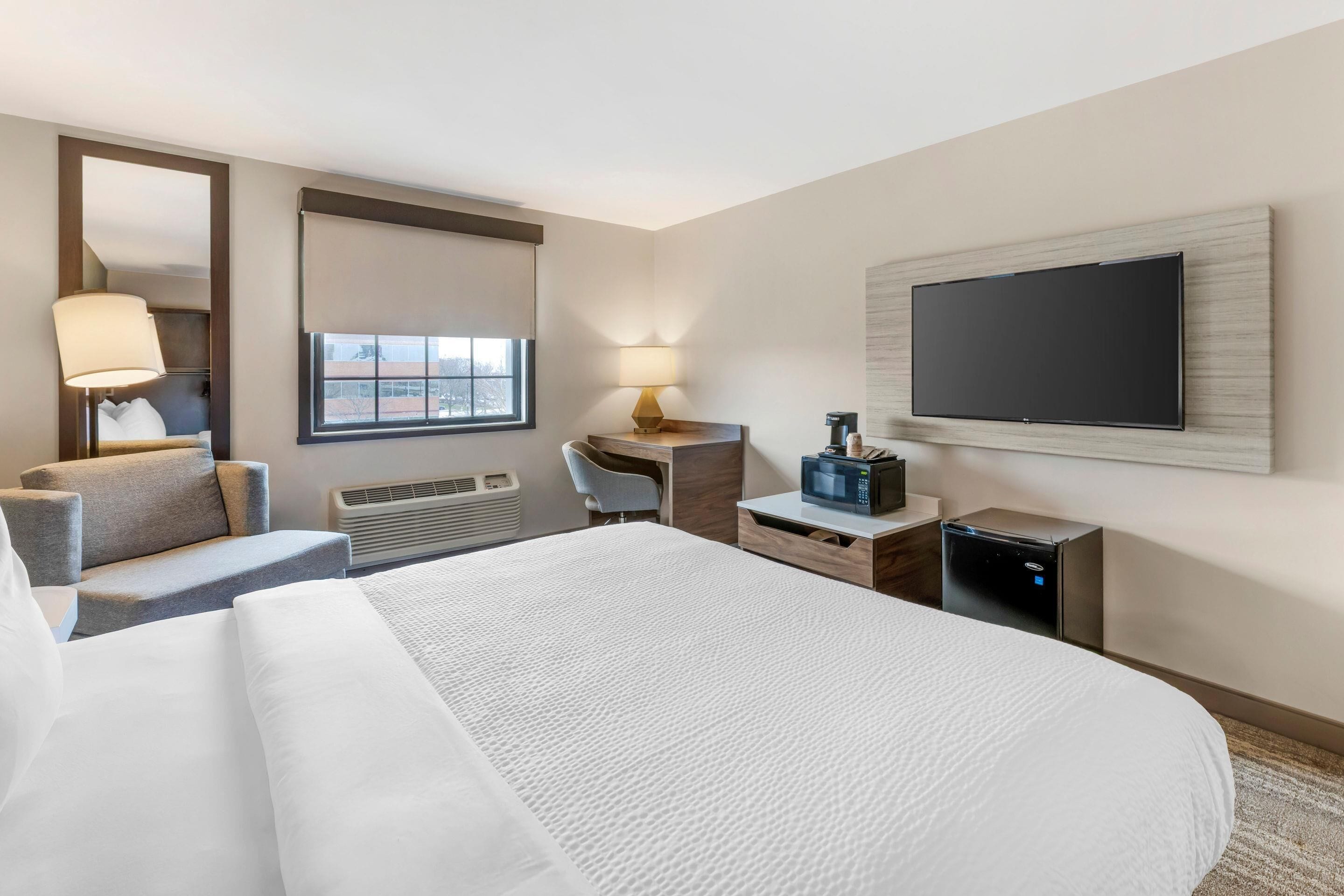 A hotel room with a large bed, a desk with a computer, a TV, and a coffee maker.