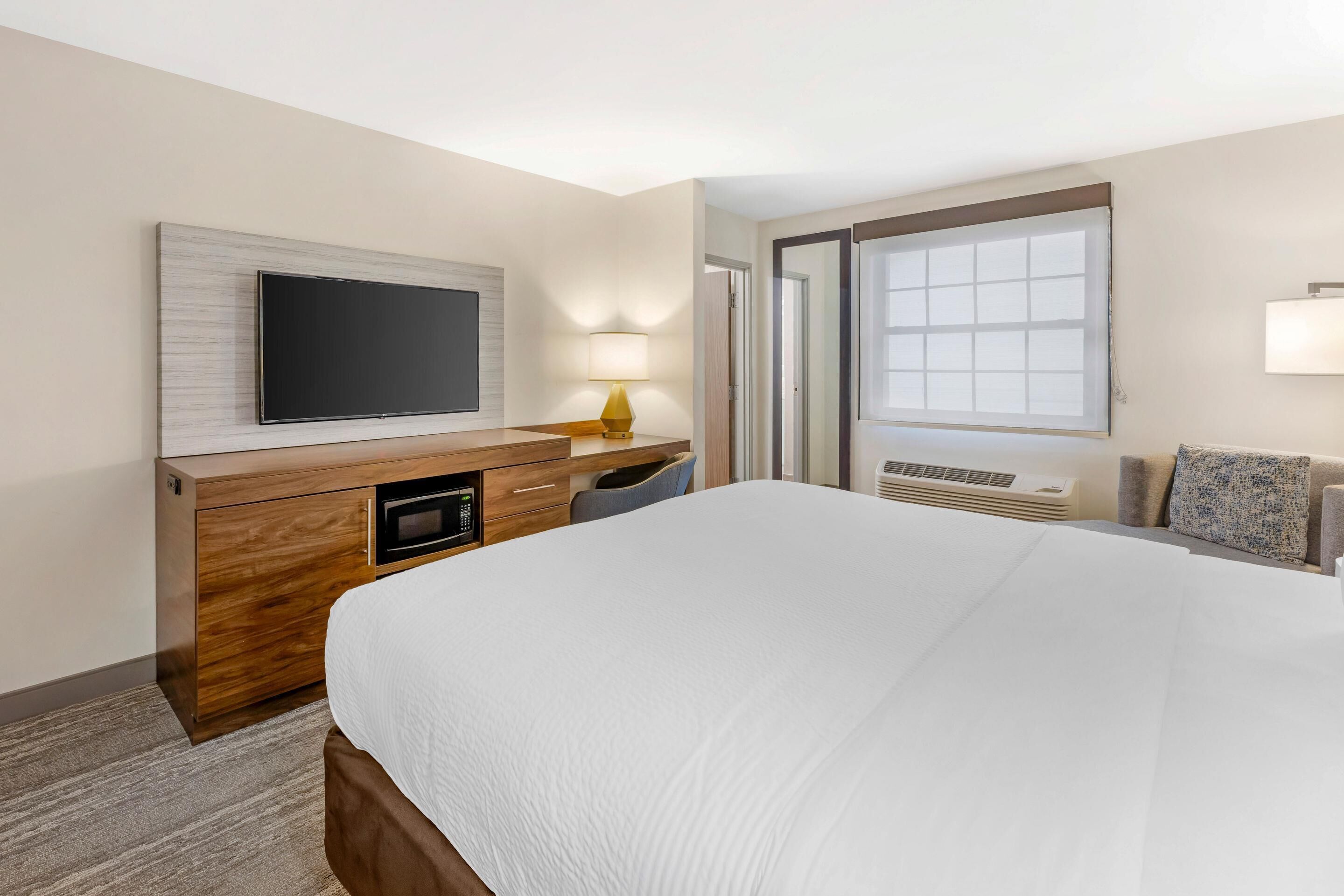 Hotelkamer met een bed, een televisie bevestigd aan een houten kast, een bureau met lamp en een raam met zonwering.