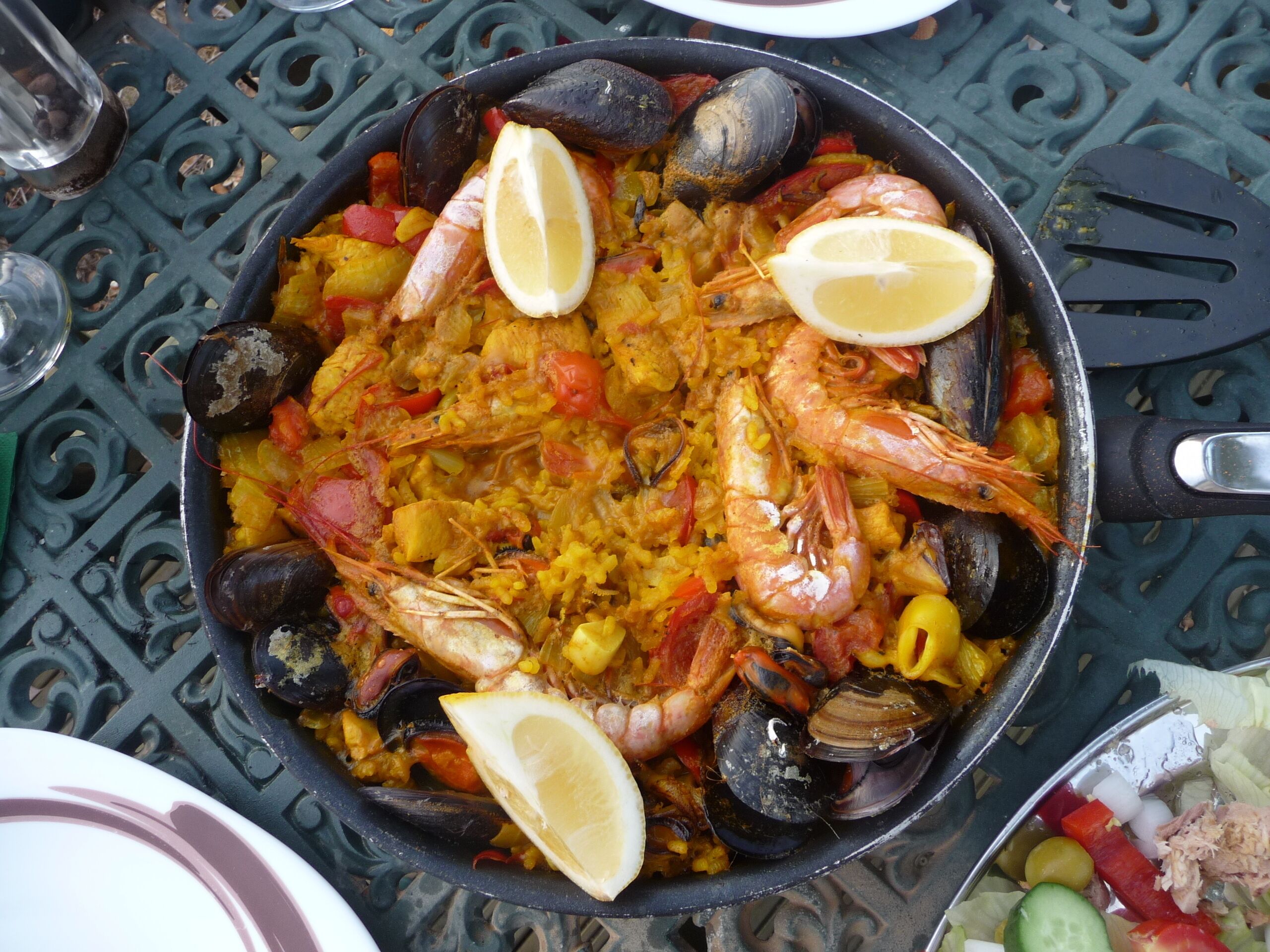 Un plato de paella de mariscos con camarones, mejillones y rodajas de limón sobre una mesa.