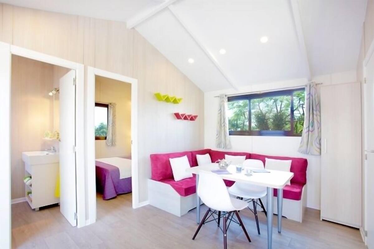 Habitació moderna amb taula de dinar blanca, sofà rosa i moble blanc.