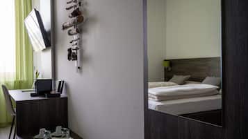 Ein Hotelzimmer mit einem Bett, einem Schreibtisch mit Stuhl, einem Spiegel und einem an der Wand befestigten Fernseher.