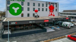 Un hotel con un gran logo verde, una parrilla y un cartel de la academia de parrilla.