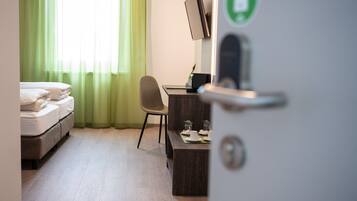 Una camera d'hotel con un letto, una scrivania con un computer e una tenda verde.