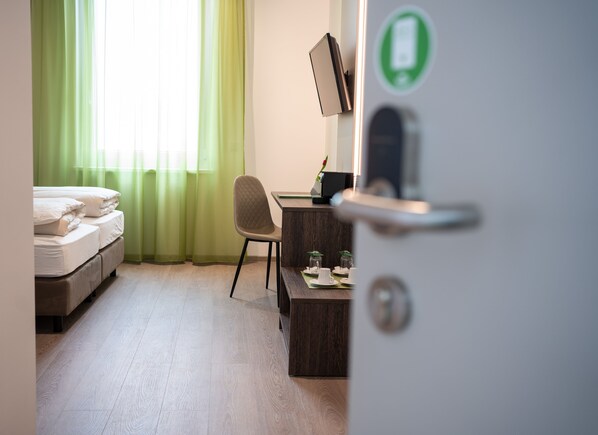 A hotel room with a bed, a desk with a computer, and a green curtain. - eee hotel Graz (Seiersberg-Pirka)