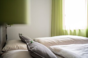 Una cama bien hecha con almohadas y una cortina verde al fondo.