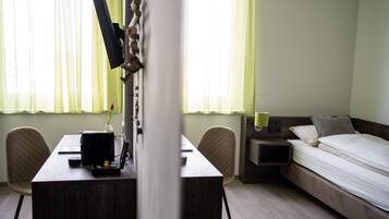 A hotel room with a bed, a desk with a computer, a chair, and a nightstand with a lamp.