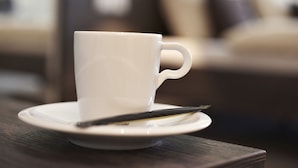 Una taza blanca sobre un plato con una cuchara sobre una mesa de madera.