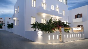 En modern vit byggnad med en skylt med texten ”MANDA” vid entrén, med ett takförsett utomhusområde med sittplatser och en väl upplyst fasad.