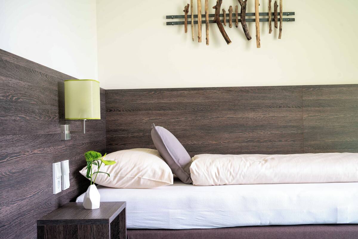 Quarto moderno com cabeceira de madeira, abajur, uma pequena planta e uma peça de arte de madeira na parede.