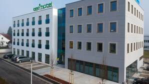 A modern hotel building with a green 'eHotel' sign, multiple windows, and a parking area with cars. - eee hotel Gunskirchen (Gunskirchen)