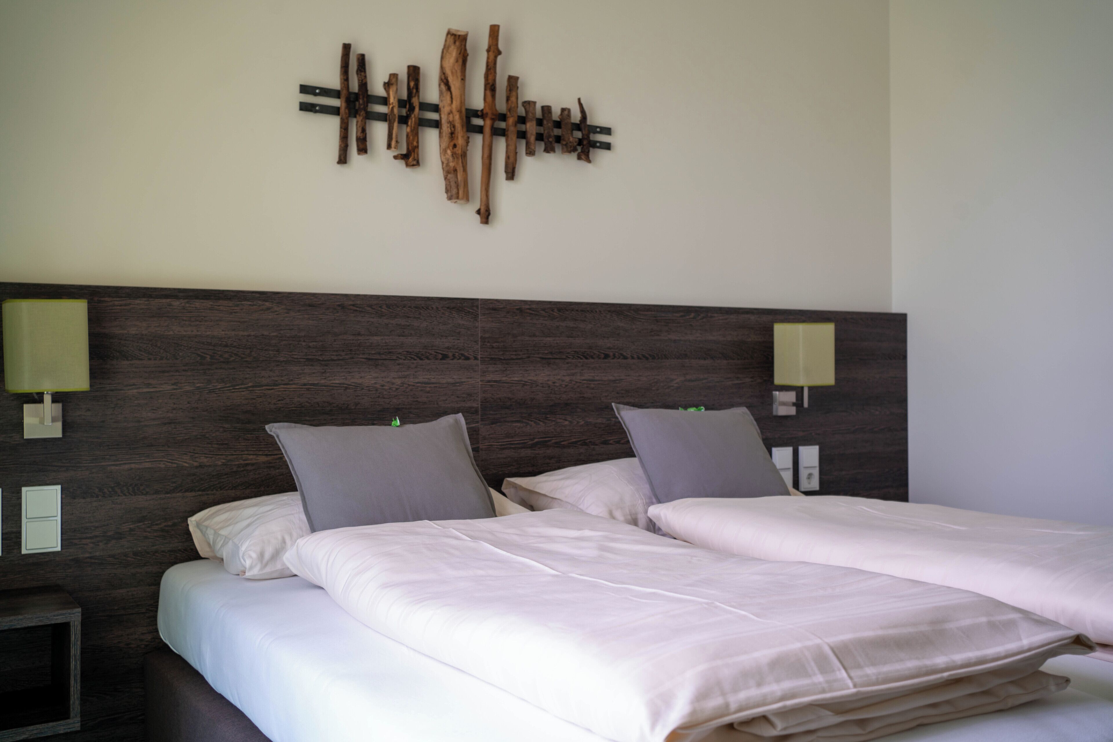 A hotel room with a large bed, two bedside tables, a wall-mounted light fixture, and a wooden wall art piece.