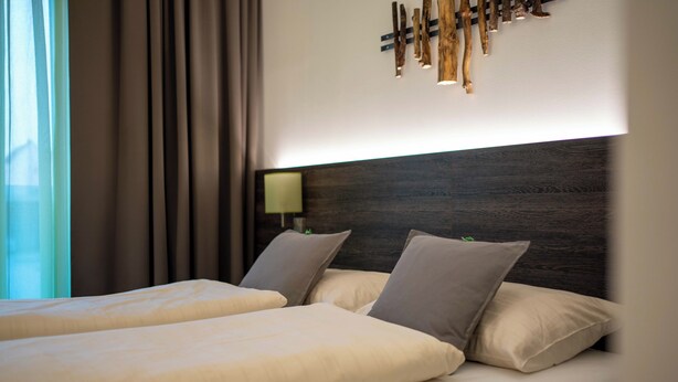A hotel room with a large bed, two pillows, a nightstand with a lamp, and a wall-mounted light fixture. - eee hotel Gunskirchen (Gunskirchen)