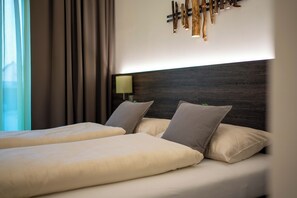 A hotel room with a large bed, two pillows, a nightstand with a lamp, and a wall-mounted light fixture.