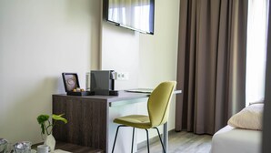 A hotel room with a desk, a chair, a bed, a TV mounted on the wall, and a window with curtains. - eee hotel Gunskirchen (Gunskirchen)