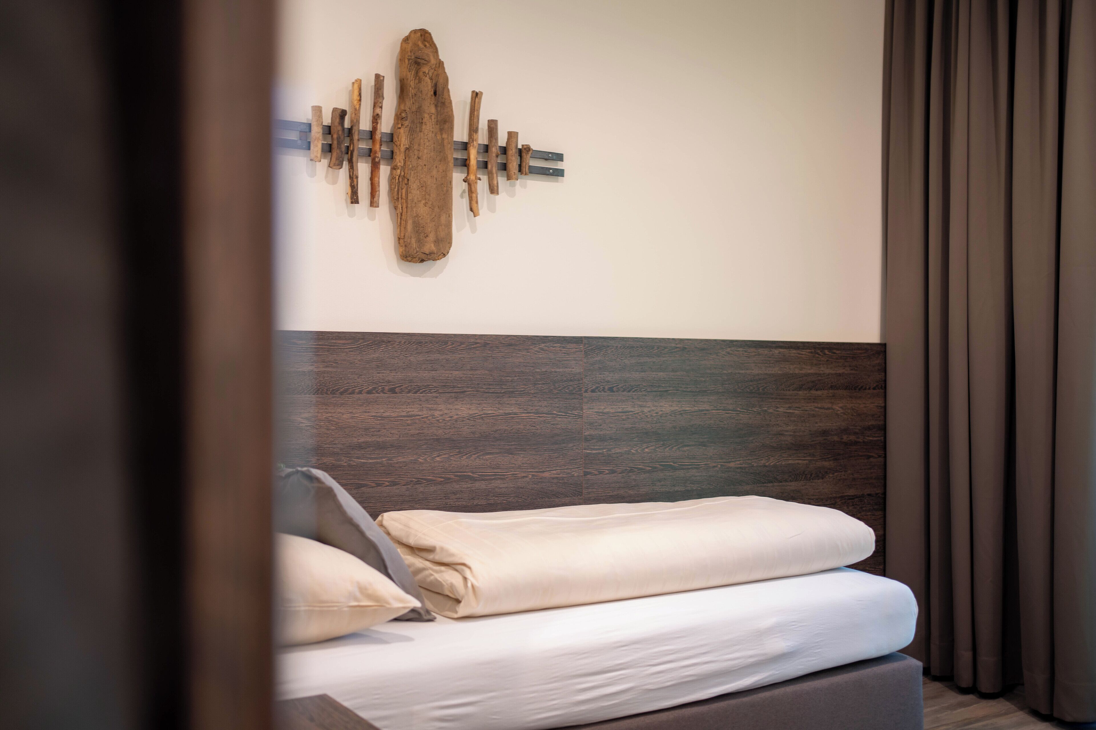 Una habitación de hotel moderna con cabecera de madera, una obra de arte abstracta en la pared y una cama bien hecha con ropa blanca.
