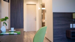 A hotel room with a wooden floor, a green chair, a white cup, and a small plant on a table. - eee hotel Gunskirchen (Gunskirchen)