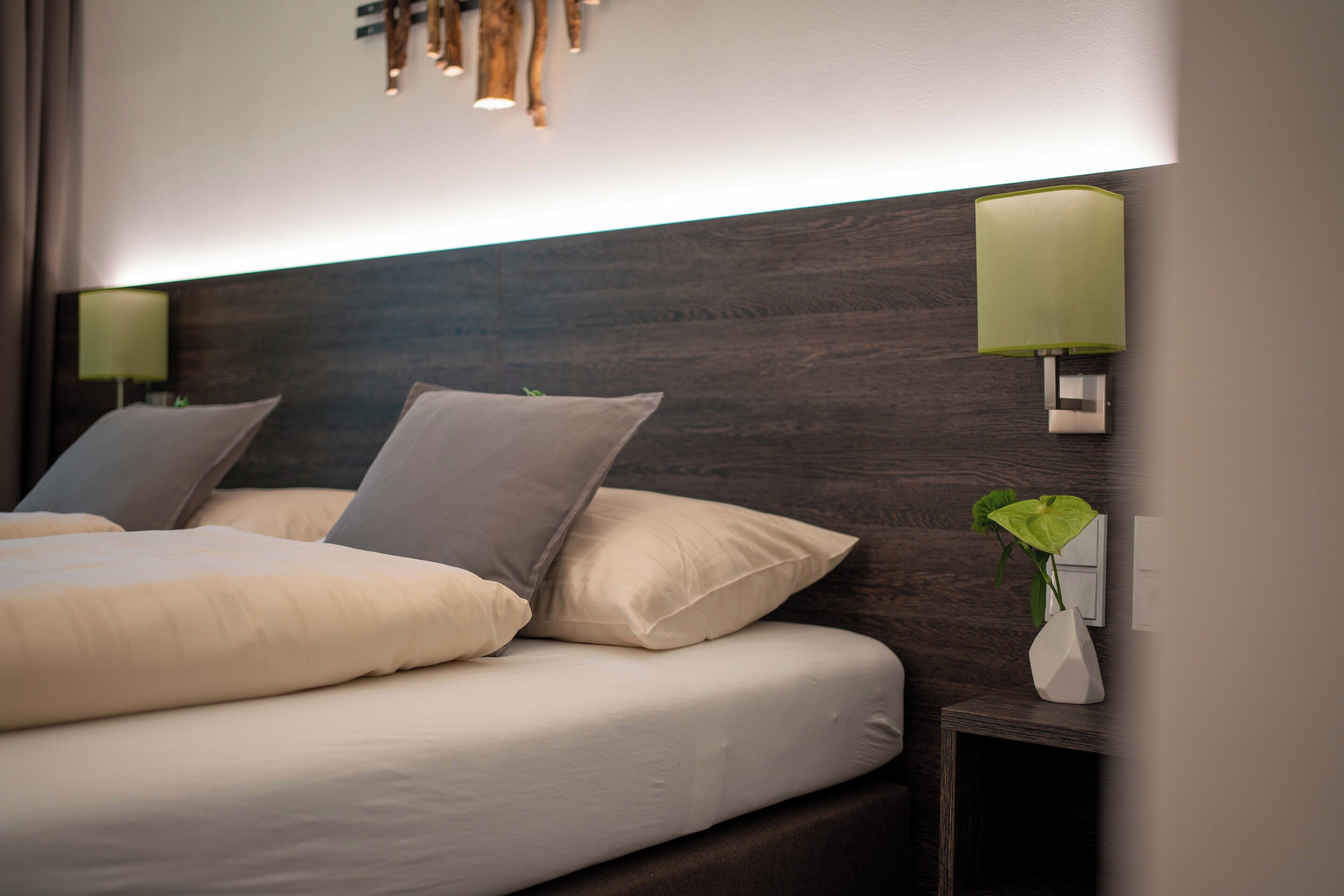 Una habitación de hotel moderna con una cama grande, dos lámparas de noche y una mesita de noche con una planta.