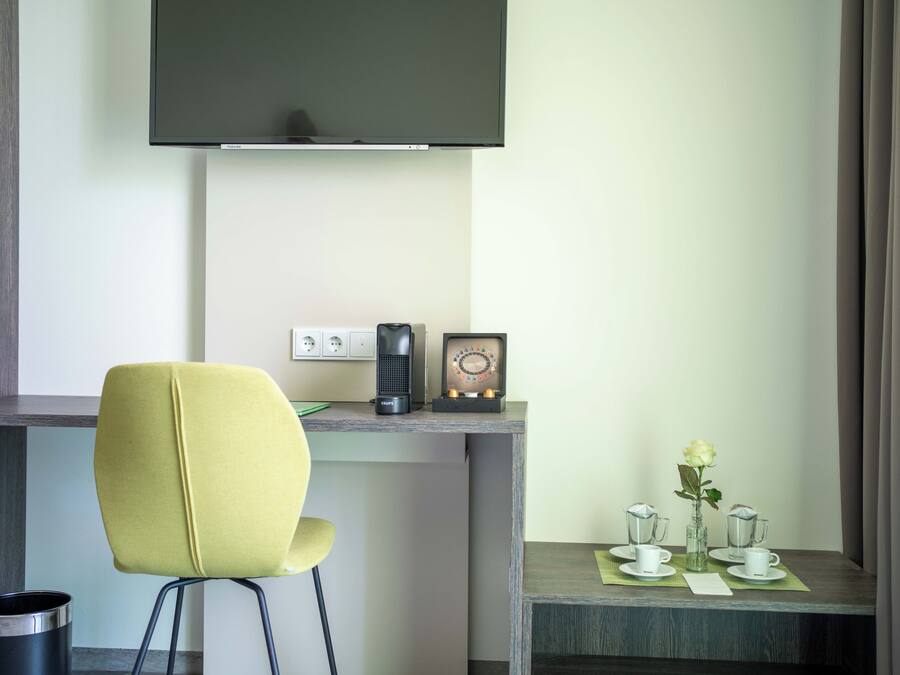 A modern hotel room with a desk, a chair, a coffee maker, a vintage radio, and a small table with a vase of flowers.
