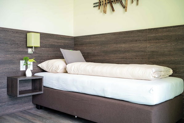 Un dormitorio moderno con un cabecero de madera oscura, una mesita de noche con una lámpara y una pequeña planta.