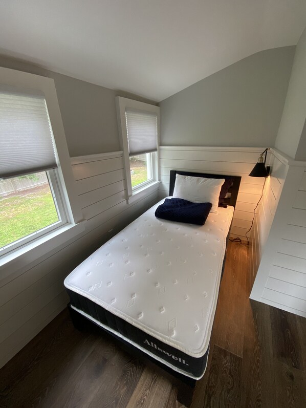 Un dormitorio con una cama individual, una ventana con persianas, una lámpara de noche y vistas al exterior.