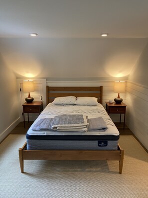 Un lit bien fait dans une chambre où se trouvent deux tables de chevet, chacune avec une lampe, et un luminaire au plafond.