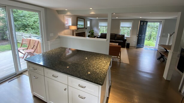 A modern kitchen with a granite countertop, white cabinetry, and a view of the backyard through large sliding glass doors. - Well Appointed Modern 3 bedroom Cape House, Fully Renovated in 2020! (Harwich)