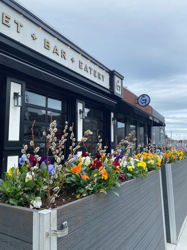 A bar and eatery with a signboard, outdoor seating with colorful flowers, and a clear sky. - Historic Victorian by the Sea (Swampscott)