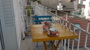 A balcony with a yellow table and blue chairs, overlooking a mountainous landscape.