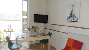 A room with a dining table, chairs, a sofa, a TV, and a window with a view of buildings.