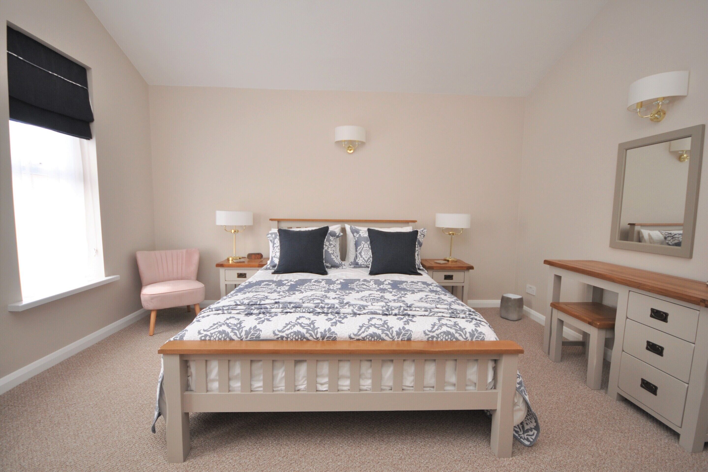 A bedroom with a bed, bedside tables, a chair, a dresser, a mirror, and a window with blinds.