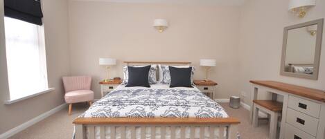A bedroom with a bed, bedside tables, a chair, a dresser, a mirror, and a window with blinds.