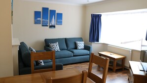 A living room with a sofa, wooden chairs, a small table, and a TV.