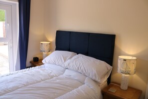 Una cama bien hecha con sábanas blancas, un cabecero oscuro y una lámpara con diseño de velero sobre una mesita de noche de madera.