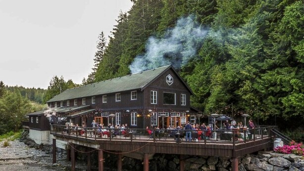 A wooden building with a deck, surrounded by trees and a rocky shoreline. - Shore 2 Please - Lower Unit,BRIGHT/Mountain views (Port Renfrew)