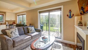 A spacious living room with a grey sofa, a glass coffee table, and a balcony with a view of the outdoors. - Shore 2 Please - Lower Unit,BRIGHT/Mountain views (Port Renfrew)